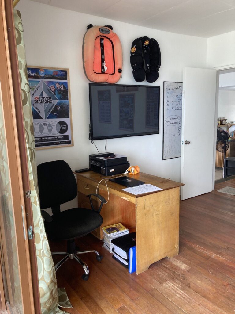 A room with a tv on a wall and a desk on the left.