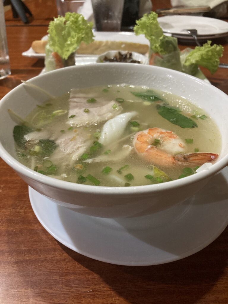 vietnamese pho soup in a white bowl on top of a brown table.