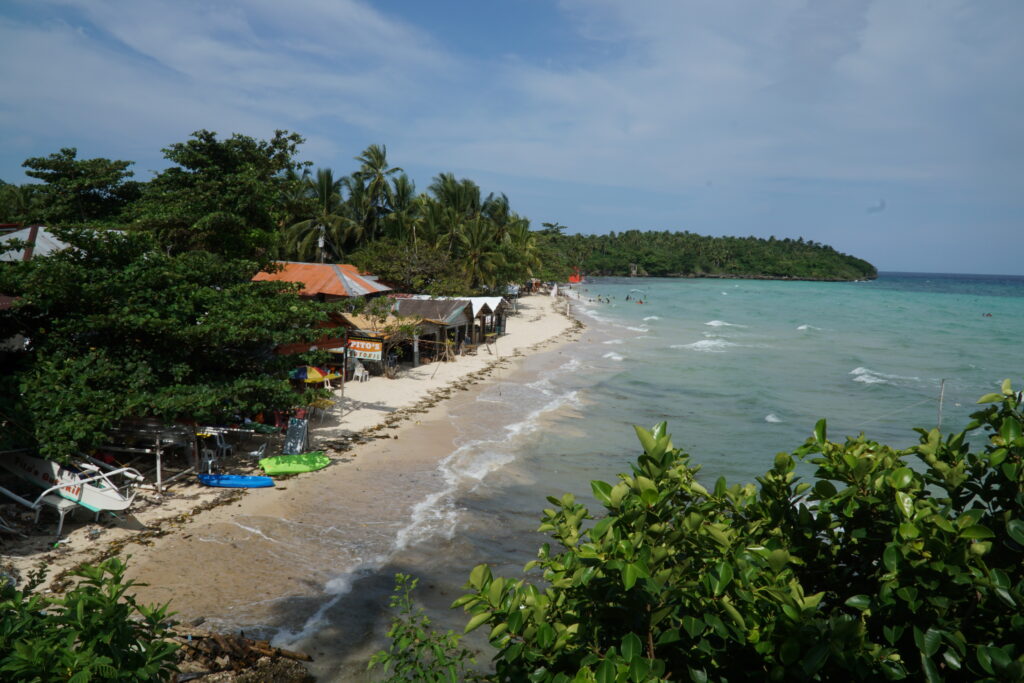 A beach on the left and on the right, a blue-green sea. Taken on top of the cliff.