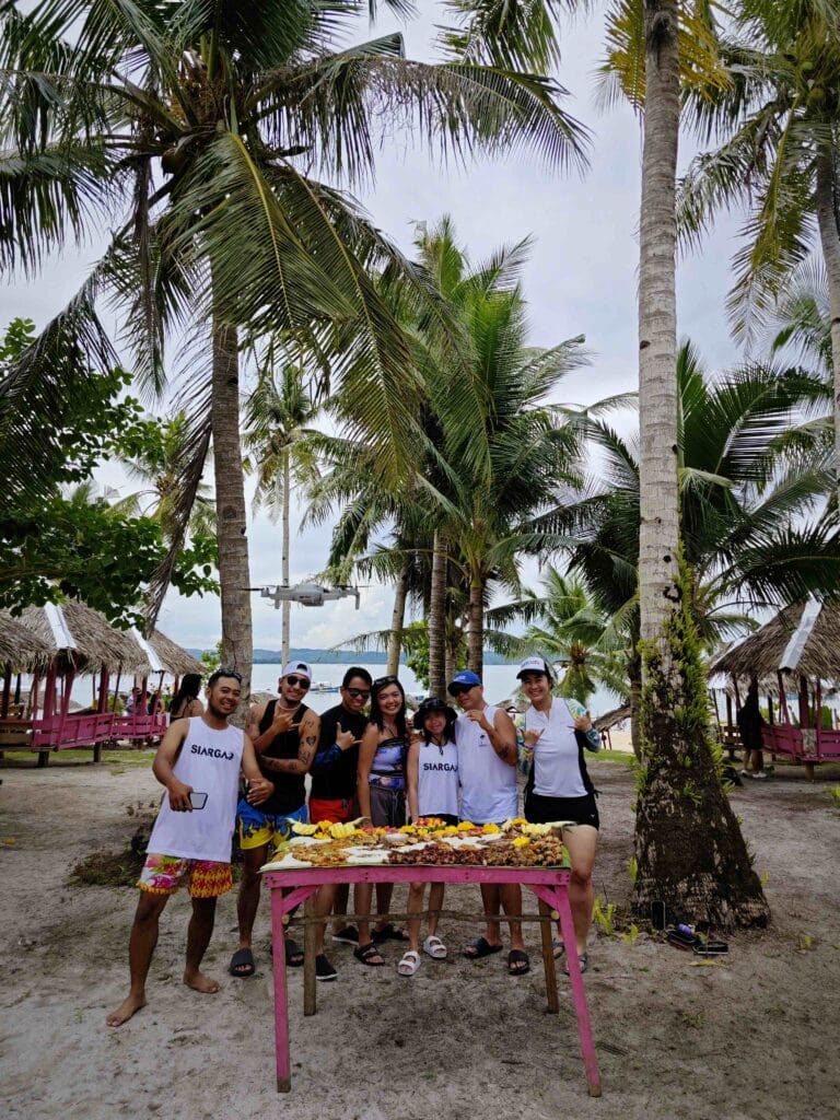 seven people taking a picture at a beach with good on a table in front.